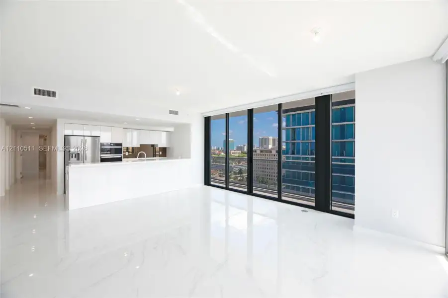 Open-concept living space featuring high-gloss tile flooring, floor-to-ceiling glass windows, and a minimalist kitchen equipped with white cabinetry and stone-surfaced countertops