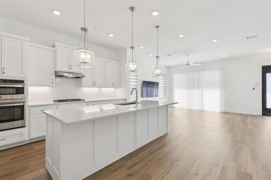 Kitchen with tasteful backsplash, white cabinets, an island with sink, pendant lighting, and recessed lighting Kitchen with tasteful backsplash, white cabinets, an island with sink, pendant lighting, and recessed lighting