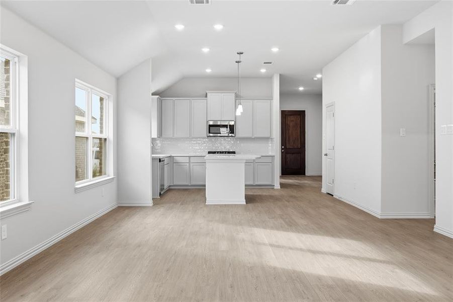 Kitchen featuring light countertops, a center island, backsplash, decorative light fixtures, and light wood-style flooring