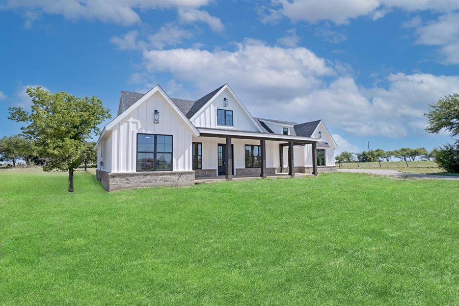 Modern farmhouse featuring board and batten siding, a porch, a front yard, and roof with shingles