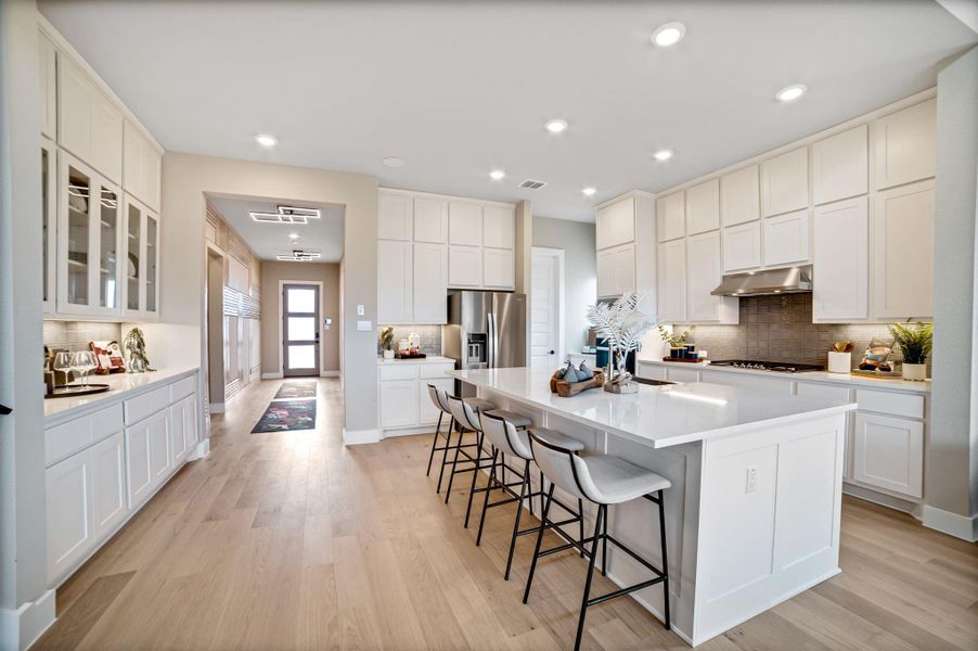 Kitchen featuring backsplash, a kitchen breakfast bar, a large island, white cabinets, and light wood-type flooring