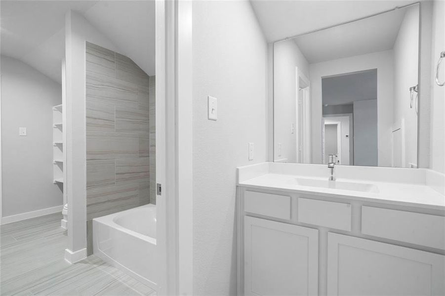 This secondary jack-n-jill bath features tile flooring, bath/shower combo with tile surround, stained wood cabinets, beautiful light countertops, mirror, sleek fixtures and modern finishes.