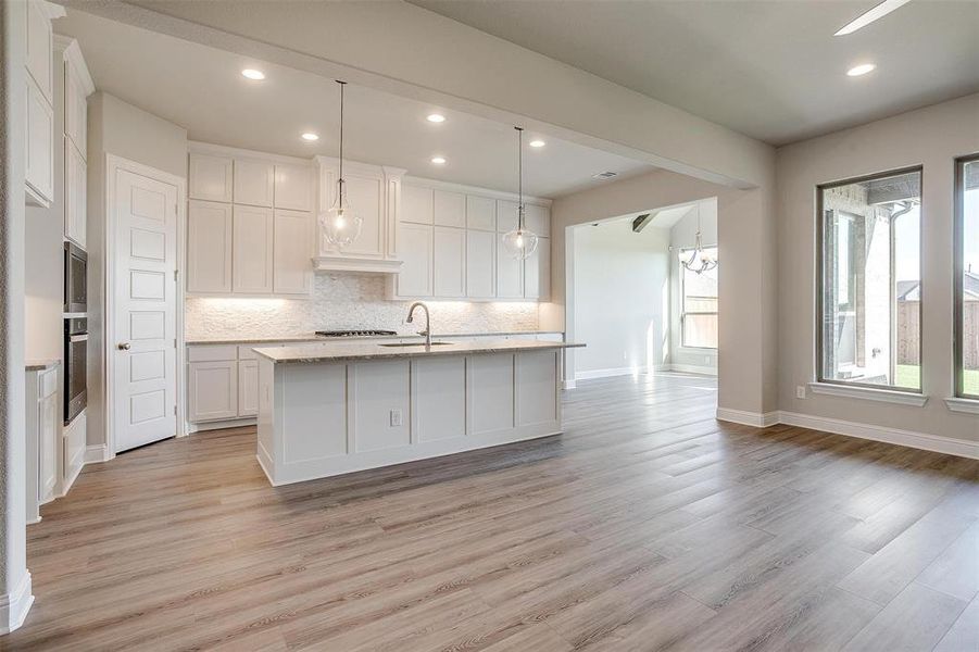 Kitchen with decorative backsplash, decorative light fixtures, a center island with sink, light hardwood / wood-style flooring, and white cabinets