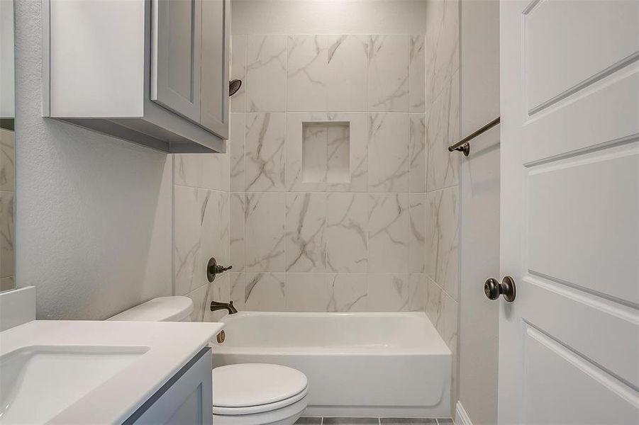 Full bathroom with tile patterned flooring, vanity, tiled shower / bath combo, and toilet