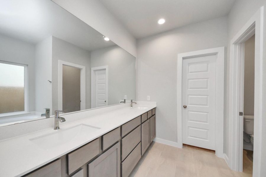 Elevate your daily routine at the elegant vanity, now equipped with double sinks, light countertops, modern hardware, and beautiful recessed lights. Sample photo of completed home with similar floor plan. Actual colors and selections may vary.