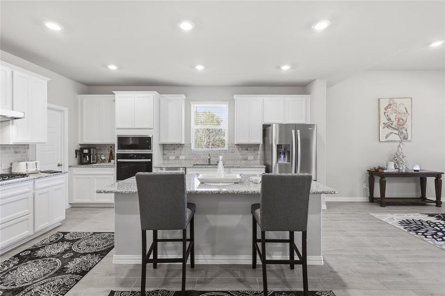Kitchen featuring an expansive island with a granite countertop, white cabinetry, stainless steel appliances, and wood-finish flooring