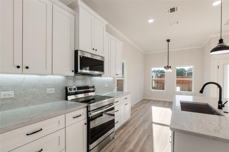 Kitchen featuring light stone countertops, appliances with stainless steel finishes, hanging light fixtures, white cabinets, and light wood-type flooring