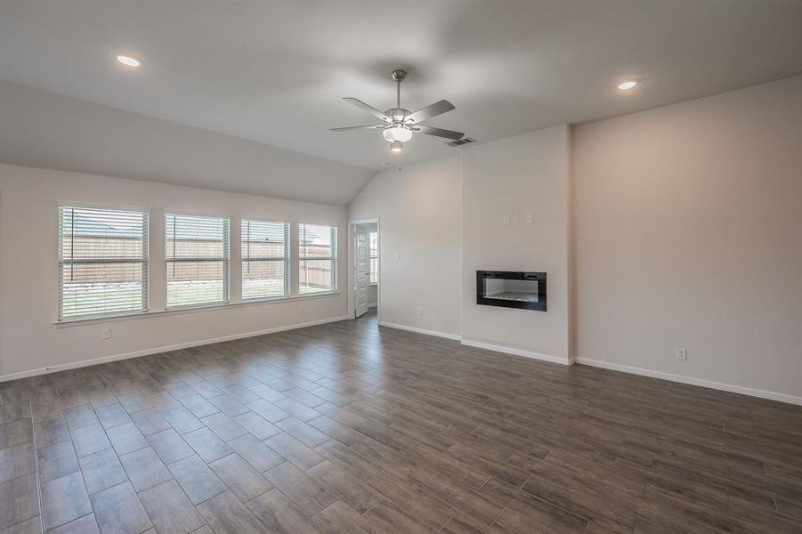 Unfurnished living room featuring lofted ceiling, dark wood-type flooring, a glass covered fireplace, a ceiling fan, and recessed lighting Unfurnished living room featuring lofted ceiling, dark wood-type flooring, a glass covered fireplace, a ceiling fan, and recessed lighting