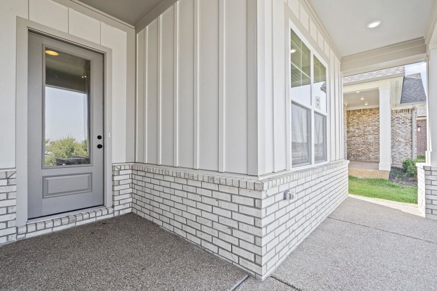 View of exterior entry featuring brick siding, board and batten siding, and a patio area