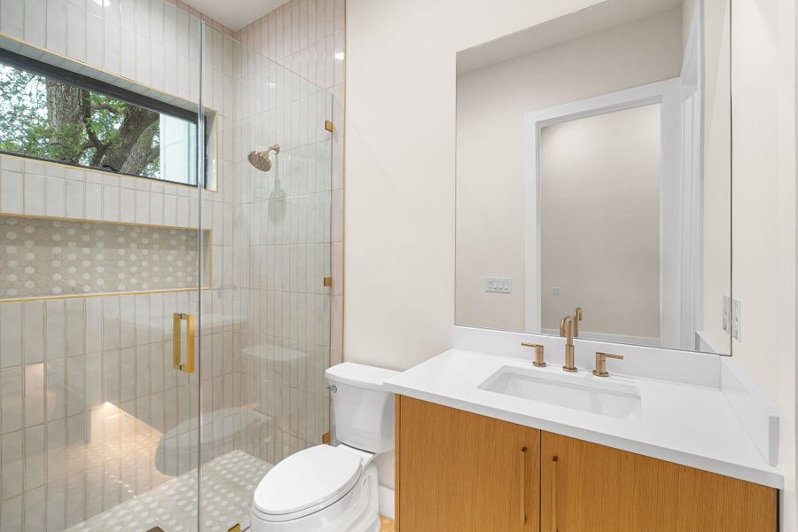 Modern bathroom featuring a wood-finish vanity with a white countertop and undermount sink, brass-finish faucet, and a frameless glass shower enclosure