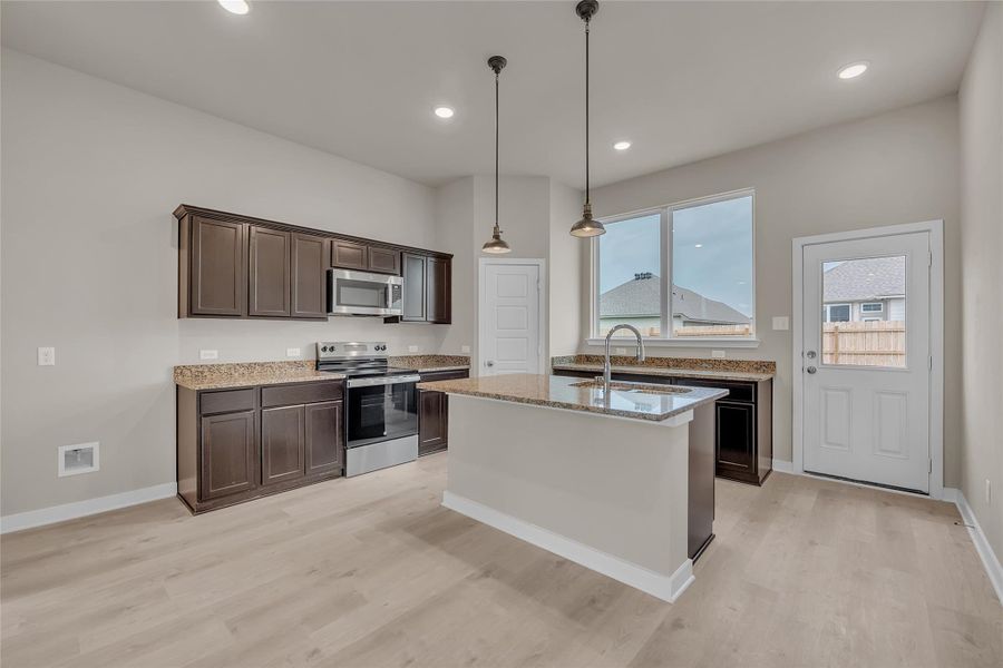 Kitchen with dark wood finish cabinets, stainless steel appliances, pendant lighting, light stone countertops, and light wood-type flooring