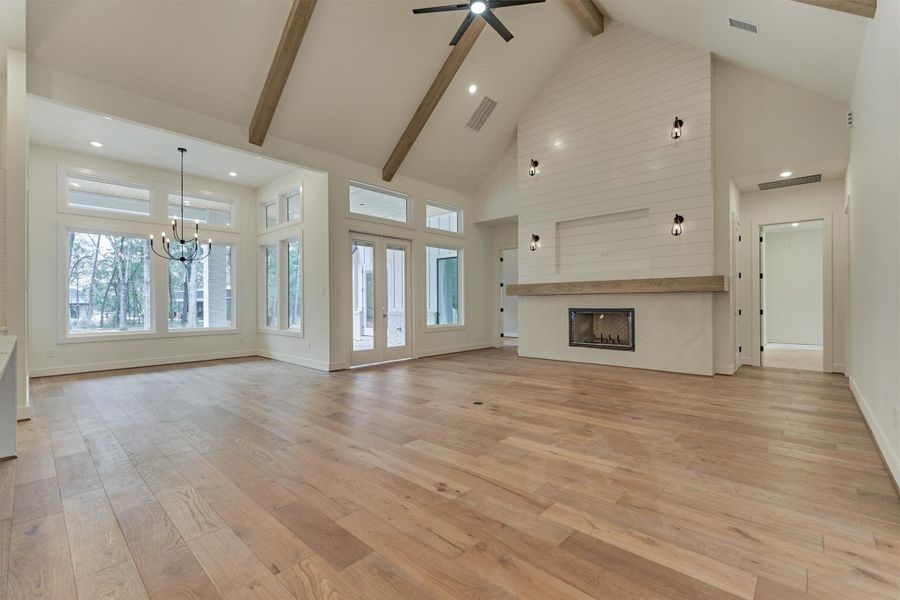 Bright and open living area featuring vaulted ceilings with wood beams, a modern shiplap fireplace, and walls of windows that showcase peaceful wooded views
