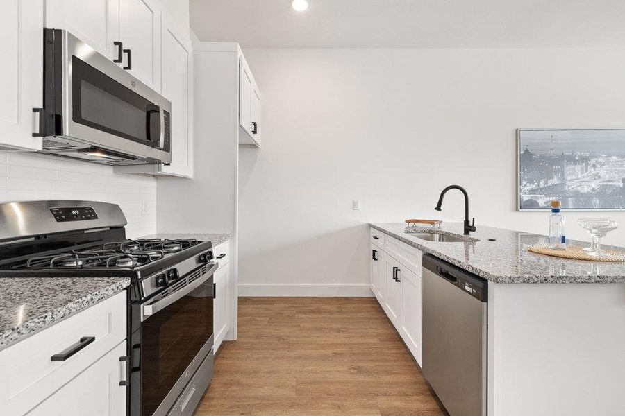 Kitchen featuring stainless steel appliances, light stone counters, a peninsula, light wood-style flooring, and white cabinets