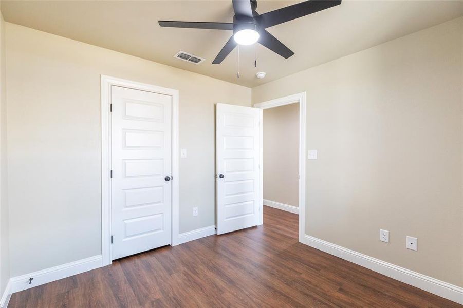 Room featuring wood-finish flooring, light-toned walls, white trim, white panel doors, and a ceiling fan with integrated lighting