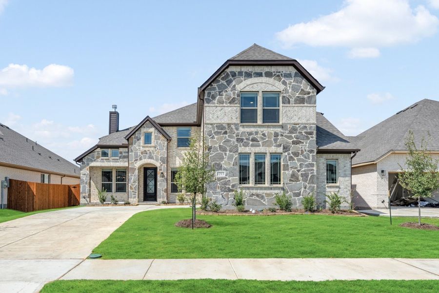 Two-story home with stone exterior, arched entry, dark roof, and manicured front lawn