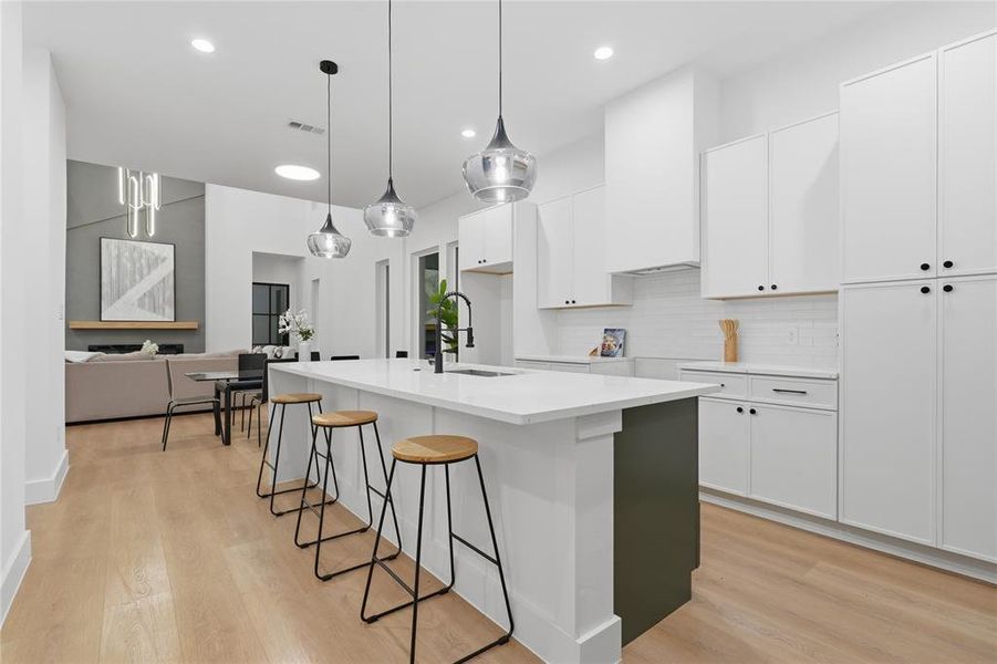 Open-concept kitchen featuring an oversized island with seating, white shaker cabinetry, white subway tile backsplash, and wood-finish flooring Open-concept kitchen featuring an oversized island with seating, white shaker cabinetry, white subway tile backsplash, and wood-finish flooring
