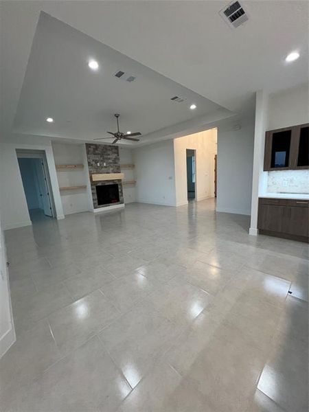 Unfurnished living room with a fireplace, built in shelves, a raised ceiling, and ceiling fan