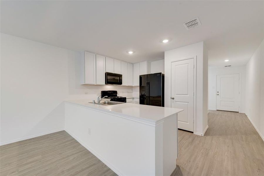 Kitchen with kitchen peninsula, light hardwood / wood-style flooring, white cabinets, and black appliances