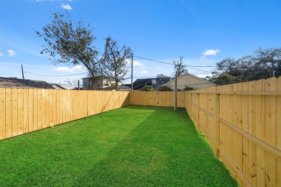A spacious backyard with lush green grass, enclosed by a wooden privacy fence, perfect for outdoor activities and gardening.