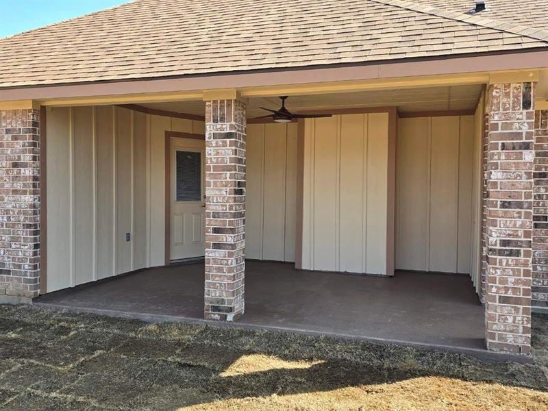Property entrance featuring a shingled roof, brick siding, and a ceiling fan Property entrance featuring a shingled roof, brick siding, and a ceiling fan