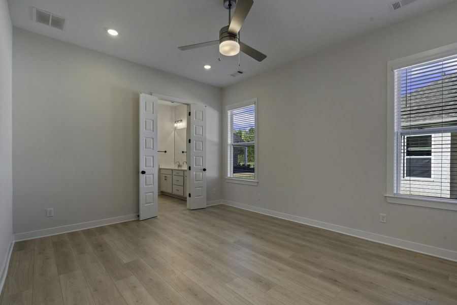 Spacious room with wood-finish flooring, two windows with blinds, and a ceiling fan with integrated lighting