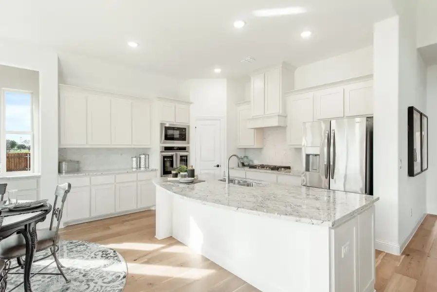 Kitchen with white cabinets, granite island, stainless steel appliances, and light hardwood floors