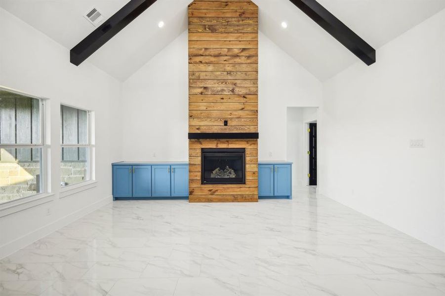 Unfurnished living room with beam ceiling, light marble finish floors, a fireplace, and high vaulted ceiling Unfurnished living room with beam ceiling, light marble finish floors, a fireplace, and high vaulted ceiling