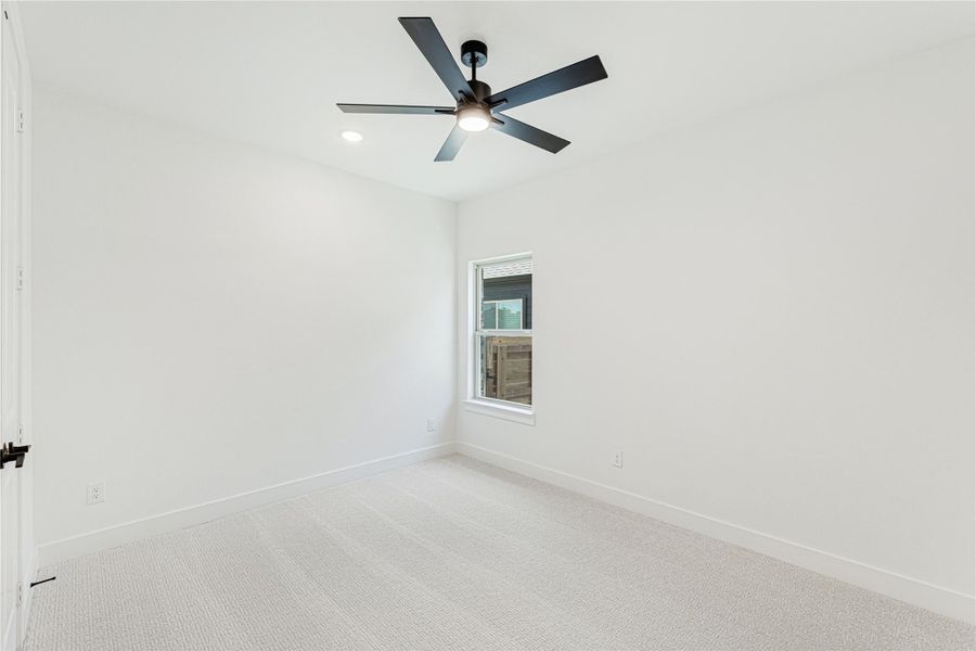 Empty bedroom with white walls, carpet flooring, ceiling fan, and single window
