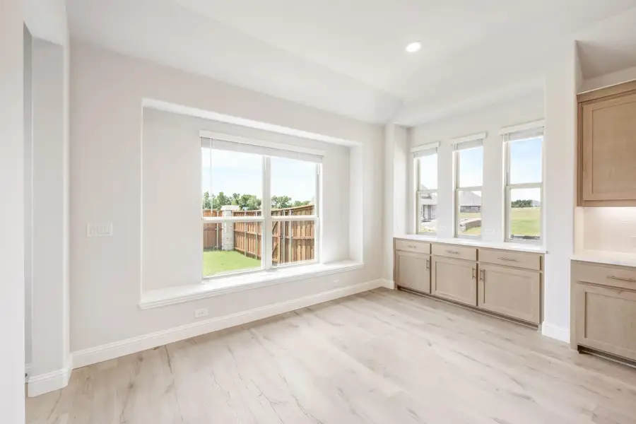 Bright dining area with light wood floors, large windows, and tan cabinets along the wall