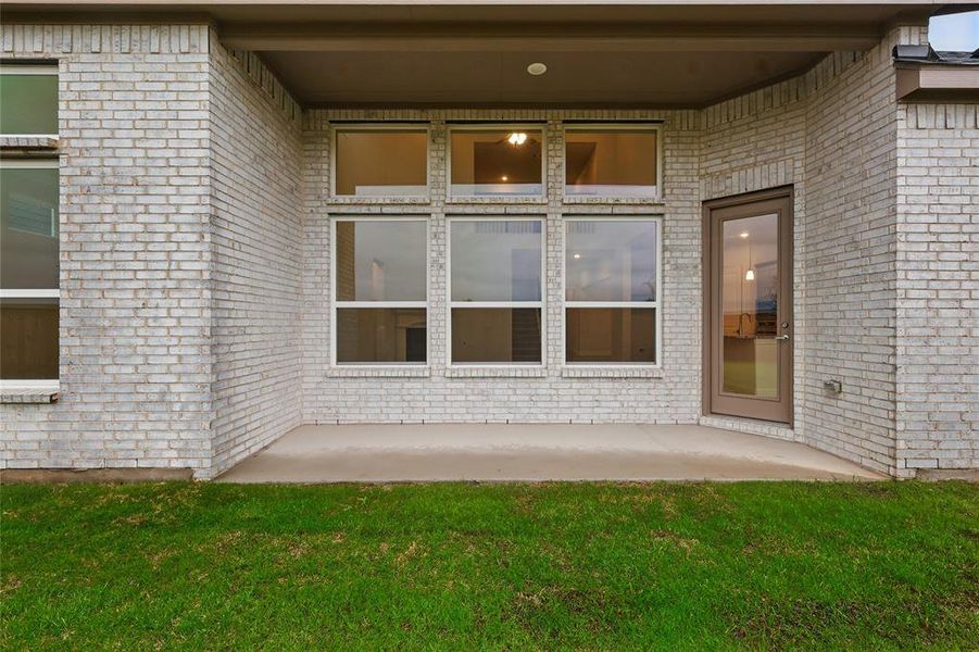 Entrance to property featuring brick siding, a patio area, and a lawn