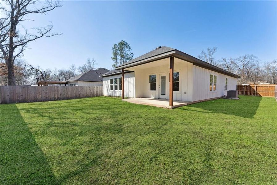 Rear view of house with central air condition unit, a patio area, and a lawn