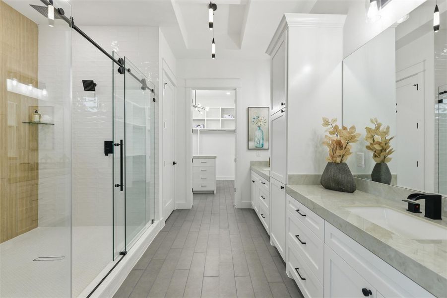 A truly grand en-suite bath showcases a glass-enclosed walk-in shower, dual vanity space, private water closet and thoughtfully layered lighting for a calm space to unwind.