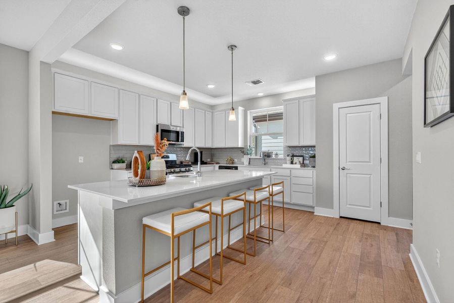 Kitchen with a breakfast bar area, decorative backsplash, white cabinets, hanging light fixtures, and light wood-type flooring