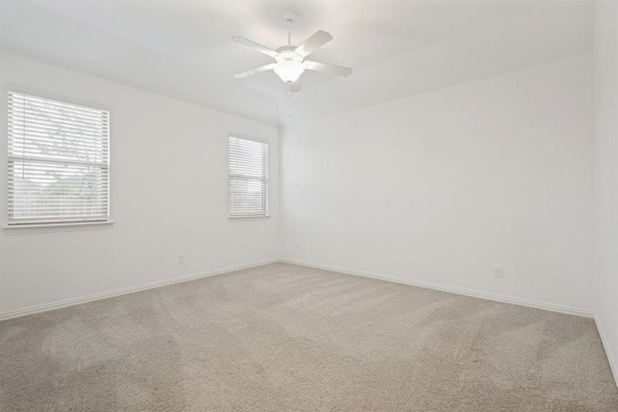 Spacious interior room featuring light-toned carpeting, white walls, two windows with horizontal blinds, and a ceiling fan with integrated lighting