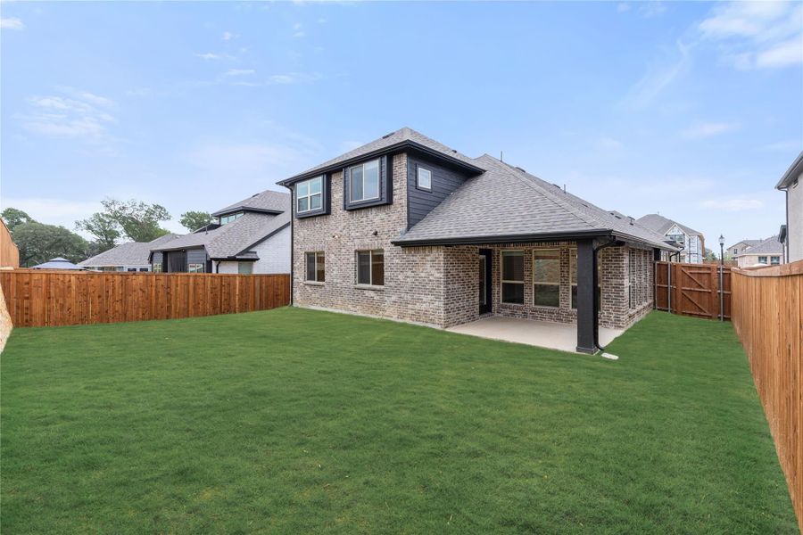 Two-story brick home rear view with covered patio, green lawn, and wood privacy fence Two-story brick home rear view with covered patio, green lawn, and wood privacy fence