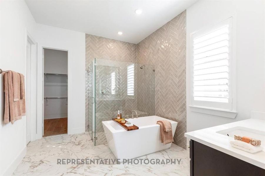 Bathroom featuring a stall shower, a walk in closet, vanity, a soaking tub, and light marble finish flooring