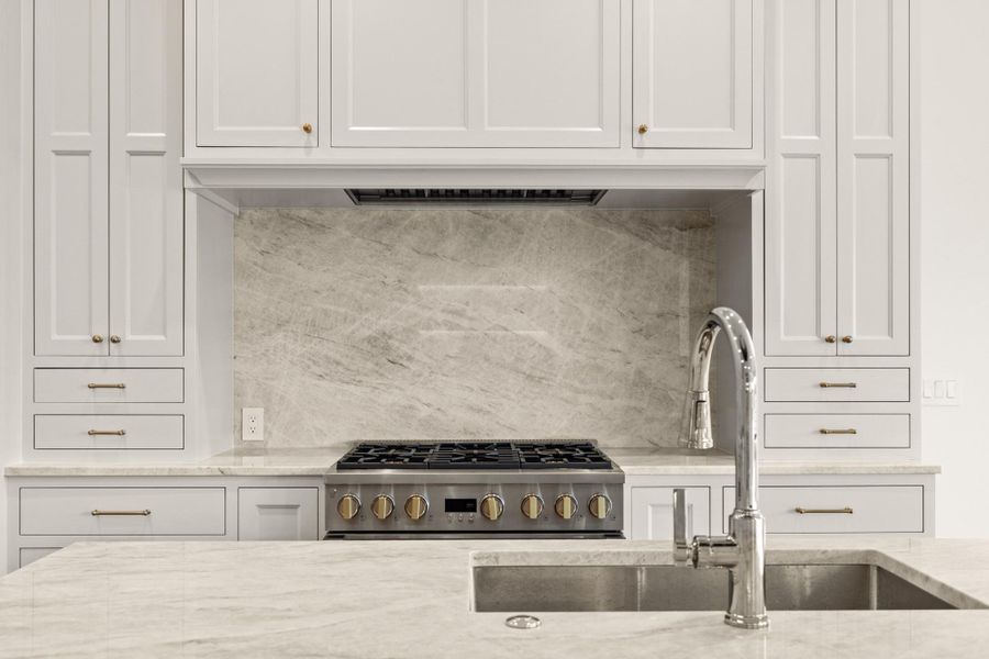 Kitchen with a sink, stainless steel gas range oven, white cabinets, and light stone countertops