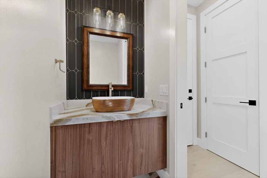 A striking powder room with a unique vessel sink and elegant tiled accent wall.