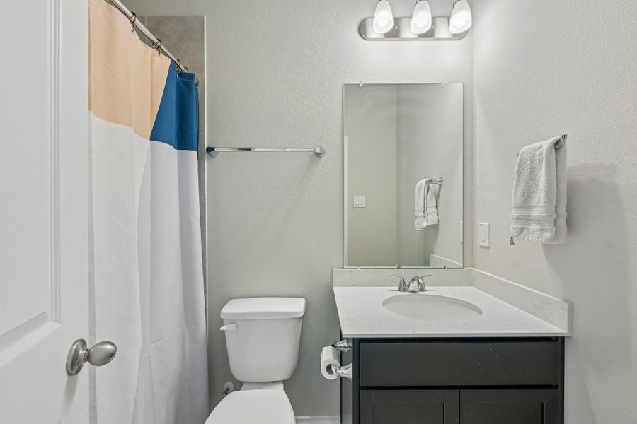 Chic bathroom featuring a modern vanity with a sleek countertop, a large mirror, and a stylish light fixture, complemented by a colorful shower curtain.