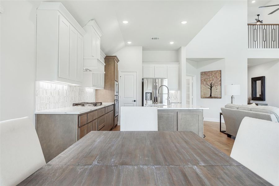 Open kitchen with white upper cabinets, wood lower cabinets, center island, and tile backsplash, open to living area