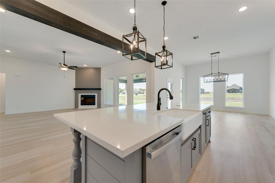 Kitchen with a center island with sink, dishwasher, light hardwood / wood-style floors, sink, and a large fireplace