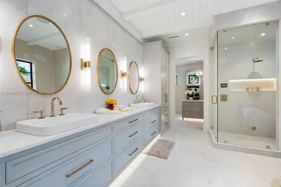 Dual-basin vanity featuring quartz countertops, large-format tile wall cladding, glass-enclosed walk-in shower with integrated recessed shelving, and custom cabinetry with gold-tone hardware Dual-basin vanity featuring quartz countertops, large-format tile wall cladding, glass-enclosed walk-in shower with integrated recessed shelving, and custom cabinetry with gold-tone hardware