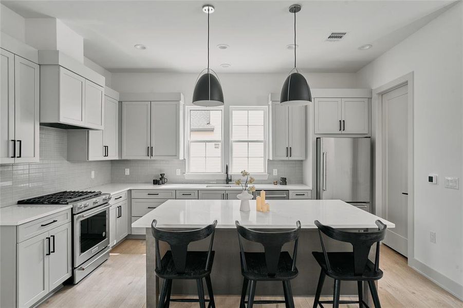 Modern kitchen featuring light gray cabinetry, stainless steel appliances, a center island with countertop seating, wood-finish flooring, and pendant lighting
