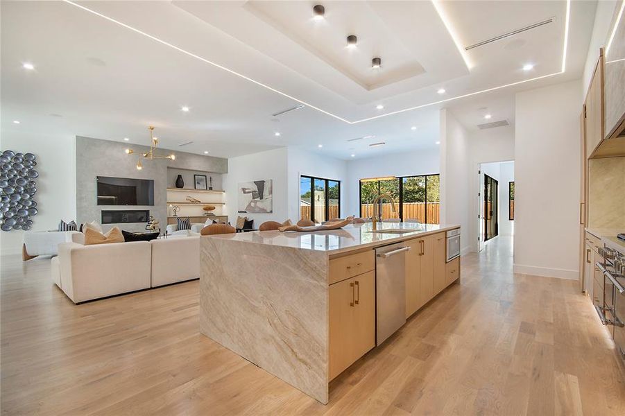 Kitchen featuring open floor plan, light brown cabinetry, a large island with sink, light stone counters, and recessed lighting