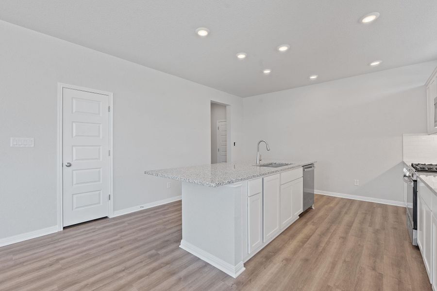 Kitchen featuring light wood-type flooring, white cabinets, a center island with sink, light stone countertops, and appliances with stainless steel finishes Kitchen featuring light wood-type flooring, white cabinets, a center island with sink, light stone countertops, and appliances with stainless steel finishes