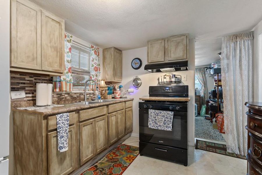 Kitchen featuring gas stove, under cabinet range hood, plenty of natural light, a sink, and a textured ceiling