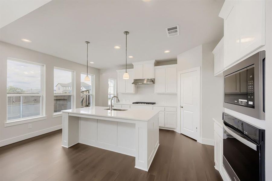 Open-concept kitchen featuring a large central island with a sink, white cabinetry, integrated stainless steel appliances, and wood-finish flooring