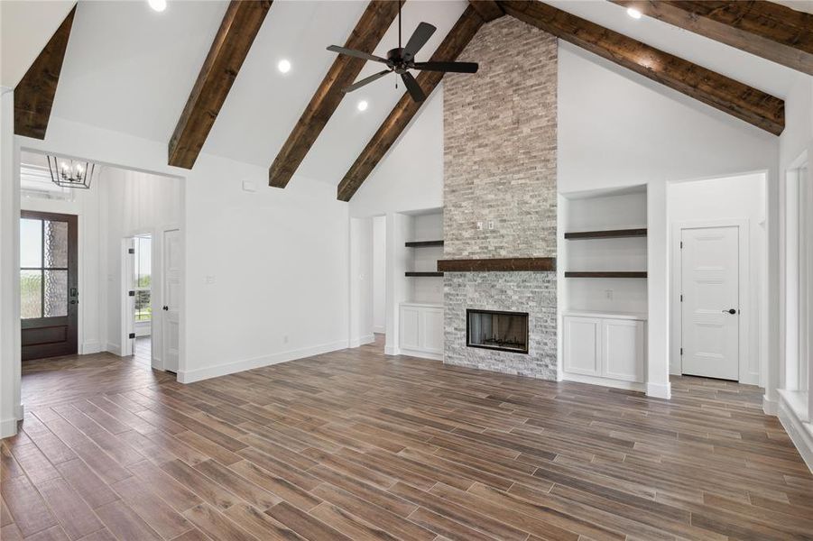 Unfurnished living room featuring a fireplace, built in shelves, ceiling fan with notable chandelier, beam ceiling, and high vaulted ceiling