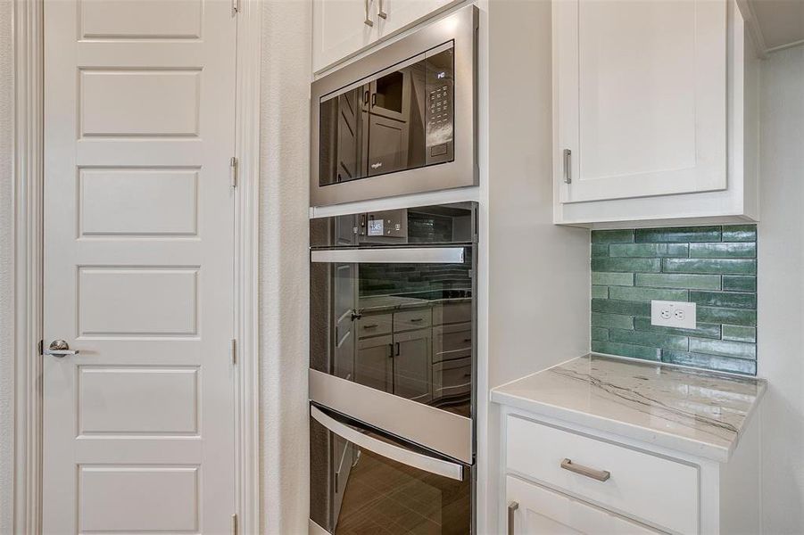 Kitchen featuring backsplash, stainless steel microwave, light stone countertops, and white cabinets