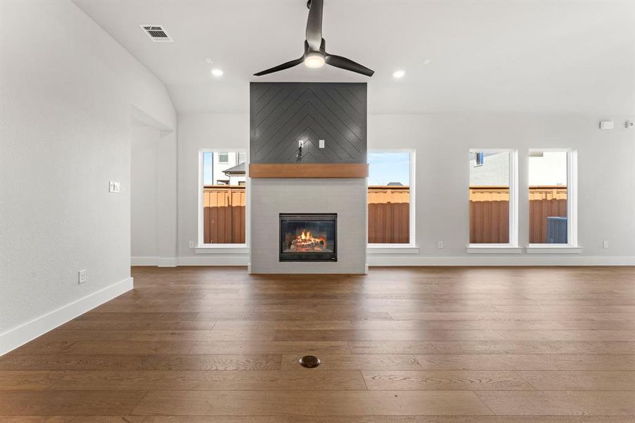 Unfurnished living room featuring ceiling fan, a large fireplace, wood-type flooring, and a healthy amount of sunlight